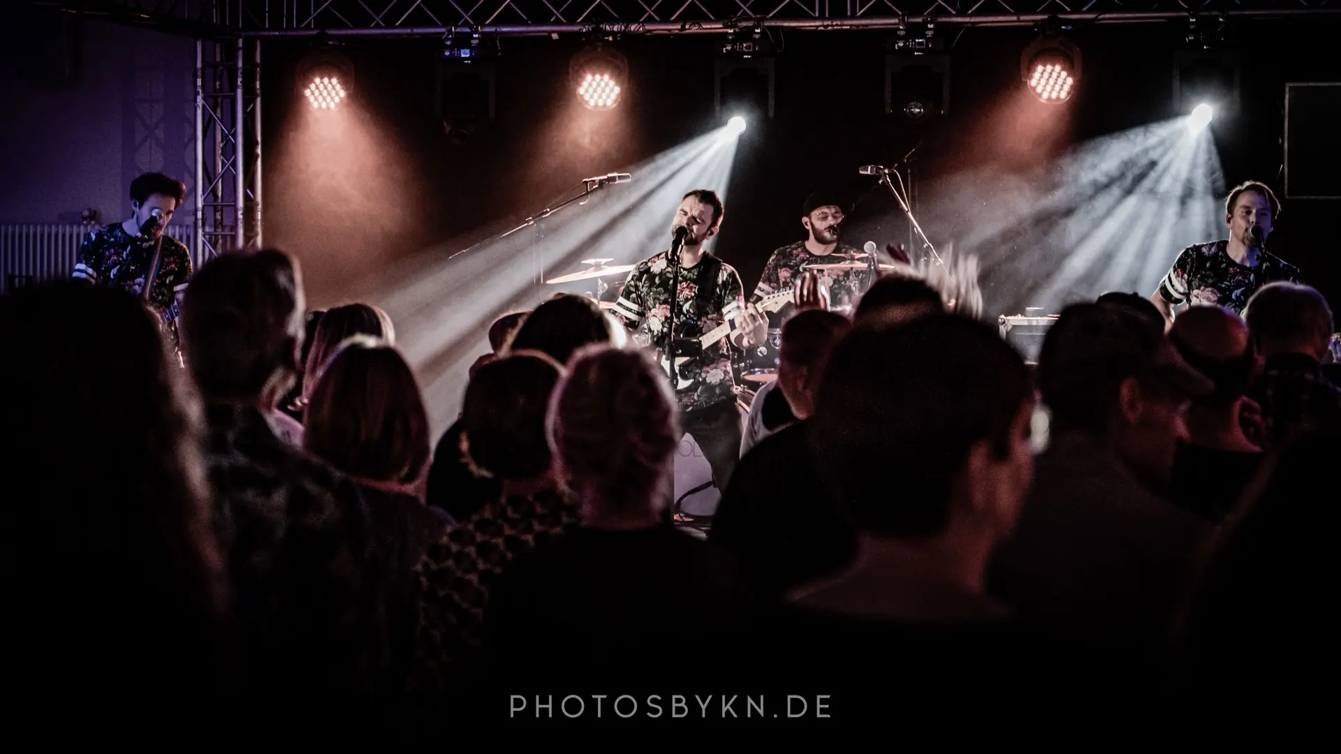 GOODBEATS live vor vollem Saal, Scheinwerfer über der Bühne, Publikum im Vordergrund