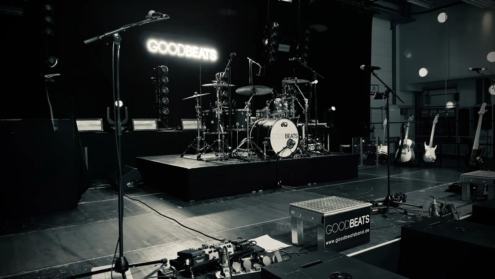 Liveband buchen: die GOODBEATS-Bühne vor der Show Liveband buchen: die Bühne der GOODBEATS vor der Show, Schlagzeug mit Bandlogo auf dem Podest, Mikrofone, Gitarren und die Leuchtschrift GOODBEATS